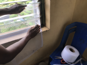 Self-adhesive mosquito mesh being fitted on a hostel window in Nigeria