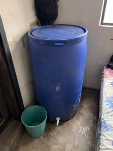Covered plastic water storage drum in a hostel room corner