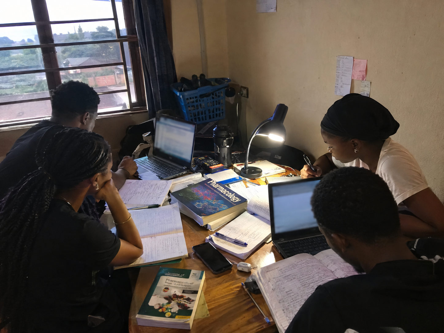 Four students studying together at a small table in a cramped common room in Nigeria